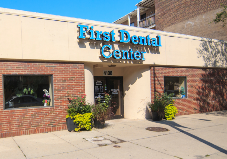Front exterior of First Dental Center with a blue sign and potted plants by the entrance.
